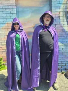 Couple in matching purple hooded cloaks with white celestial trim