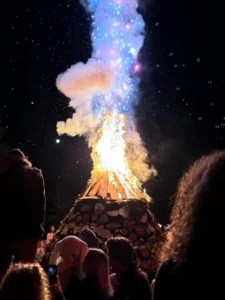 Bonfire by Ashley MacFarlane A lit bonfire with its tip glowing red, yellow and blue sparkles