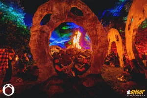 couple-in-head-by-zac-mac Two people relax by a bonfire inside a large, carved stone archway at a nighttime festival.