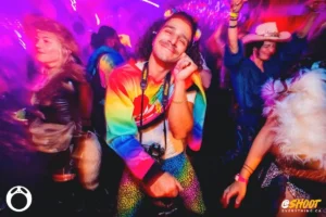 derek-by-zac-mac Man in colourful outfit dancing at a vibrant music festival with blurred crowd